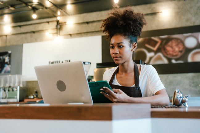 Restaurant manager holds tablet and looks at a laptop on the counter