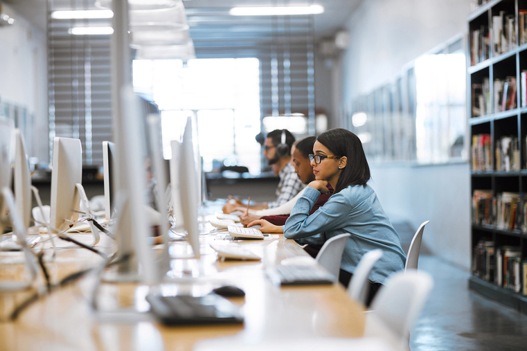 Group of students, appearing to be engaged in research assignment, work on desktop computers in modern computer lab