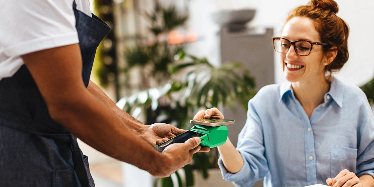 Seated customer uses smartphone to make cashless payment on handheld point of sale device